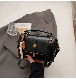 Detail of black faux leather bag featuring a gold ring buckle and wood bead tassel