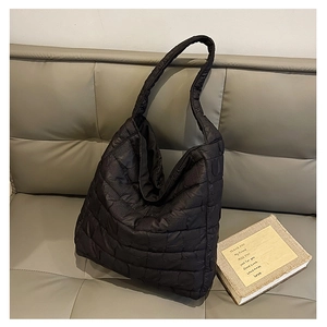 Detail of black quilted puffer tote bag fabric texture on white leather sofa