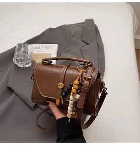 Detail of a brown vintage leather Boston bag featuring colorful bead tassel and gold hardware
