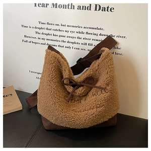 Detail of plush brown teddy fleece bucket bag with bow and embroidered text on black stand