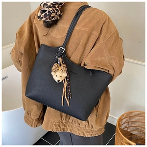 Detail of black litchi grain leather tote bag with a leopard print bear charm
