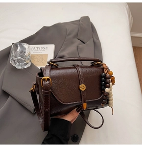 Close-up of deep brown oil-wax leather shoulder bag with vintage texture and wooden beads