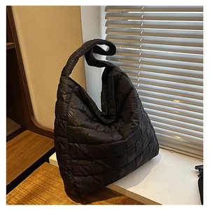Detailed close-up of a black quilted tote bag with square texture and wide strap