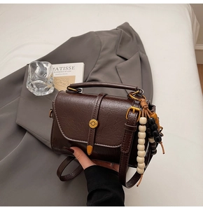 Detail of dark brown leather crossbody bag featuring unique wooden bead pendant decor