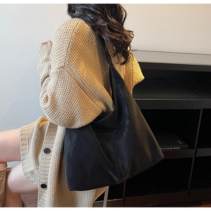 Detailed side view of a black matte crescent tote bag worn by a model in a cozy cardigan
