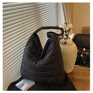 Macro detail of black quilted puffy tote bag featuring textured square stitching patterns