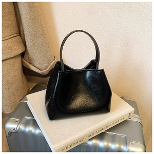 Détail d'un sac seau en cuir noir avec poignée haute posé sur une valise métallique