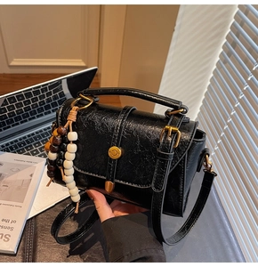 Detail of black Boston bag with vintage beads charm and textured leather in soft sunlight