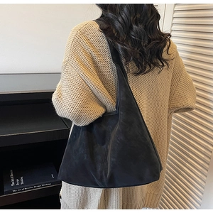 Side view of black matte suede tote bag worn by a model in a beige sweater