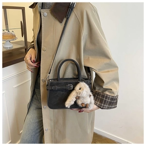 Detail of black leather handbag featuring a plush white bunny charm on a beige trench coat