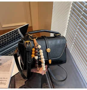 Detail of a black textured crossbody bag featuring vintage gold hardware and wooden beads