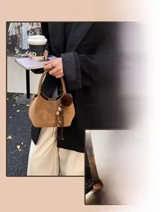 Détail d'un sac seau en daim caramel avec un pompon décoratif et des franges