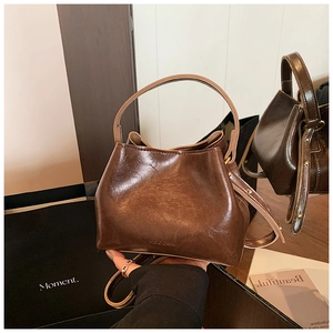 Détail du sac seau en cuir marron brillant montrant la poignée ronde et la bandoulière fine