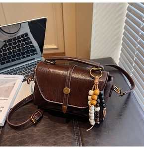 Detailed close-up of dark brown oiled leather bag with metal clasp and colorful wood beads