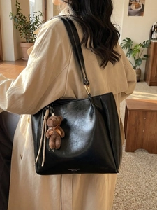 Grand sac cabas noir en cuir avec pendentif ours, porté par un mannequin dans un intérieur