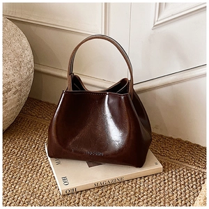 Détail du sac seau marron foncé brillant avec logo HOCOMU posé sur un magazine