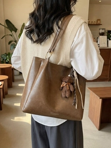 Sac fourre-tout marron en cuir avec breloque ours et doubles anses dans un café