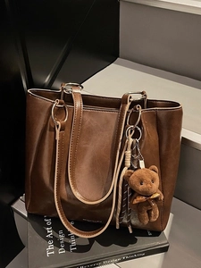 Sac fourre-tout vintage marron foncé avec breloque ours en peluche sur un socle de livre
