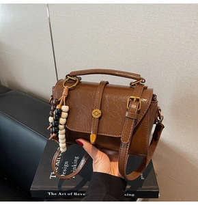 Detail of vintage brown leather square bag with buckle and contrast wood bead charm