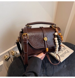 Close-up of retro dark brown leather crossbody bag with wooden bead charm and metal disc