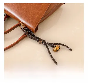 Detail einer braunen Ledertasche mit geflochtenem Anhänger und Vintage-Glocke