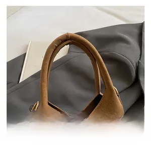 Dettaglio dei manici tondi di una borsa a secchiello in pelle scamosciata marrone e oro
