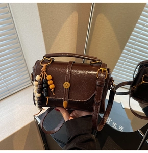 Detail of dark brown leather crossbody bag with vintage oil finish and wooden bead tassel