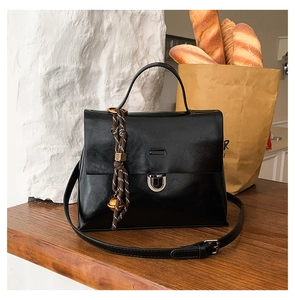 Detail der schwarzen Handtasche mit geflochtenem Griff und Goldglöckchen auf Holztisch