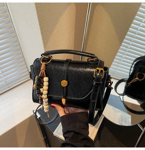 Detail of black textured leather bag with gold buckle and wooden beaded accessory