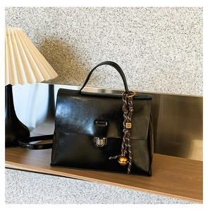 Nahaufnahme der schwarzen Ledertasche mit Silberverschluss und geflochtenem Anhänger