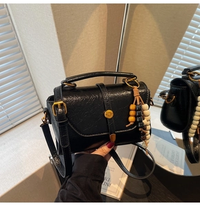 Detail of black wrinkled leather square bag with golden buckle and wooden bead charm