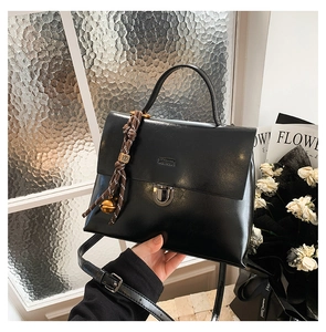 Detail einer schwarzen glänzenden Handtasche mit Metalldrehverschluss und Glockenanhänger
