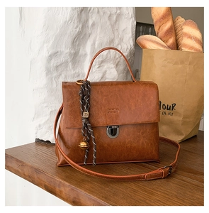 Detailaufnahme der braunen Retro-Handtasche mit Metallschließe und Glockenanhänger