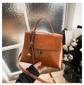 Detail einer braunen Vintage-Lederhandtasche mit Metallschloss und gewebtem Anhänger