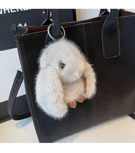 Detail of grey plush bunny charm with metal ring attached to a black leather tote bag