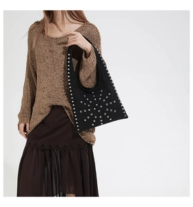 Detail of a black studded tote bag styled with a warm brown knit sweater and pleated skirt