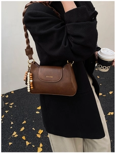 Detail of dark brown leather shoulder bag featuring woven strap and beaded wood charm