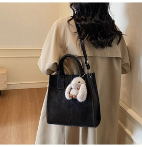 Detail view of black suede tote bag with plush bunny charm on a beige trench coat