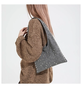 Close-up of gray suede tote bag featuring silver metal rivets and textured finish