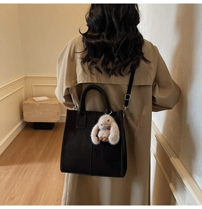 Detail of a black matte tote bag with a grey rabbit plush charm on a shoulder strap