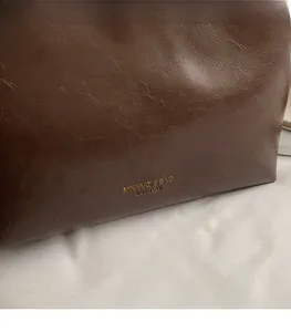 Close-up of brown oil-wax leather texture with gold stamped logo on the tote bag