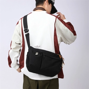 Detail of a large black nylon crossbody bag with side drawstring pocket and adjustable strap