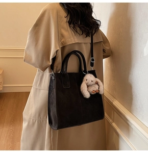 Close-up of black suede tote bag with a white plush rabbit pendant on a camel coat