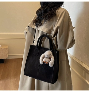 Detail of black matte tote bag with plush rabbit charm worn with a beige trench coat