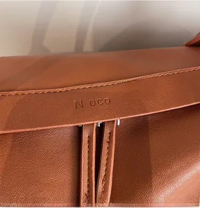 Detailed macro view of brown pebbled leather texture and embossed N OCO logo on tote bag