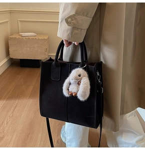 Detailed close-up of a black leather tote bag with a cute beige plush bunny charm