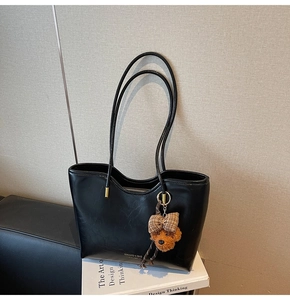 Close-up of black leather tote bag with gold hardware and a cute teddy bear charm