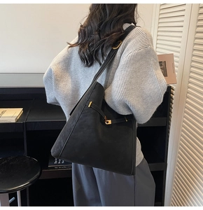 Detail of black suede bucket bag with gold metal buckle closure on a stylish shoulder strap