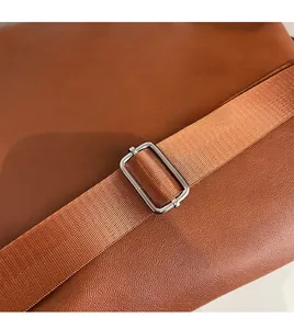 Detail of brown leather bag featuring smooth adjustable woven strap and silver metal buckle