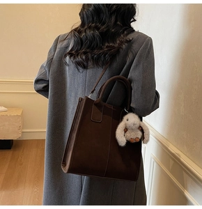 Detail of dark brown faux suede tote bag with plush bunny charm on a grey wool coat